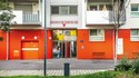 Außenansicht des Eingangbereichs. Das Erdgeschoss hat eine rote Fassade.