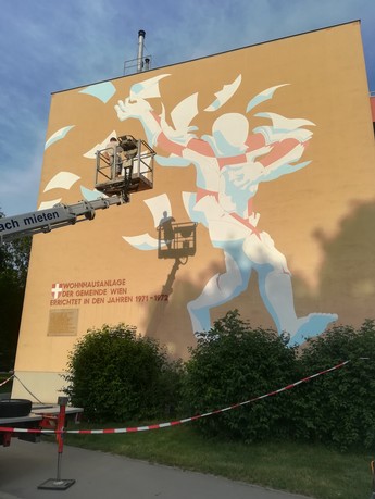 Foto von einer Hauswand, die ein Grafitti von einem abstrakten Menschen zeigt, der aus vielen weißen Papier-Zetteln besteht. 