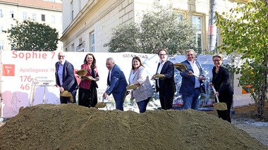 Eine Gruppe an Personen steht vor einem Erdhaufen und hält Schaufeln mit Erde zur Kamera.