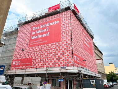 Baustelle mit großflächigem Wiener-Wohnen-Banner „Das Schönste in Wien? Wohnen!“ an einem eingerüsteten Gebäude.
