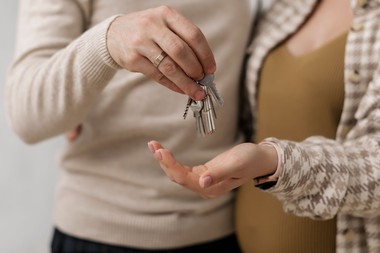 Nahaufnahme zweier Personen: Eine Person übergibt einen Schlüsselbund mit mehreren Schlüsseln an die andere, die die Hand zum Entgegennehmen geöffnet hält. Die Gesichter sind nicht sichtbar. Die Szene vermittelt eine Schlüsselübergabe, beispielsweise im Zusammenhang mit einer Wohnungs- oder Hausübergabe.
