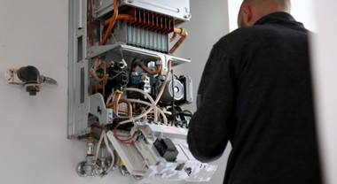 Das Foto zeigt einen Mann in einem schwarzen lang-arm T-Shirt von hinten, der an den Kabeln einer Erwärmepumpe arbeitet. 