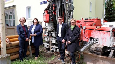 Das Foto zeigt Wohnbaustadträtin Kathrin Gaal mit drei anderen Personen auf einer Baustelle vor einem Haus mit hellgelber Fassade. 
