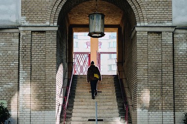 Eine Frau von hinten geht die Stiege hinauf durch einen Torbogen.