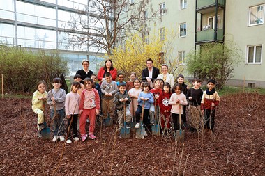 Das Bild zeigt eine Schulklasse und vier erwachsene Personen mit Schaufeln in einem gepflanzten Wald in einem Gemeindebau.