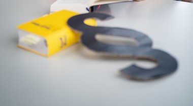 Das Foto zeigt einen gelben Kodex und ein dekoratives Paragraphen-Zeichen, das darüber gelegt ist. 