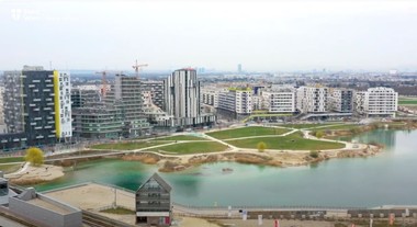 Foto mehrere Hochhäuser vor einem See und einer Grünfläche