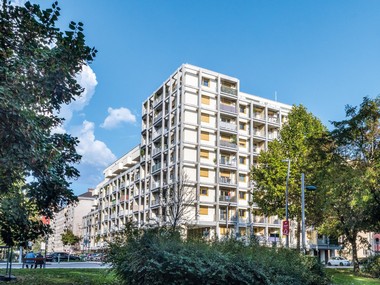Ansicht des Gemeindebaus in der Dr-Natterer-Gasse mit über 6 Stockwerken. Das Gebäude hat eine moderne Ästhetik.