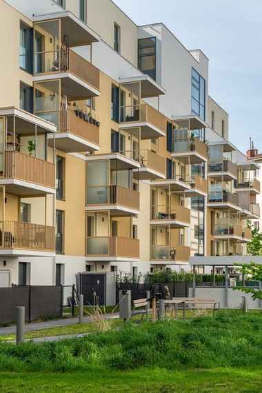 Innenhof des Gemeindebaus. Die Stockwerke haben jeweils einen überdachten Balkon und im Erdgeschoss sind kleine Gärten und öffentliche Sitzmöglichkeiten