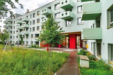 Außenansicht des neuen Gemeindebaus Wildgarten-Hof. Vor dem sechsstöckigen Gebäude befindet sich eine große Wiesenfläche.