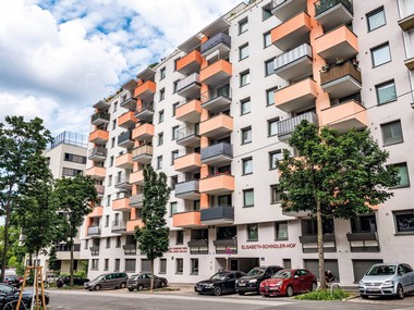 Außenansicht des Gemeindebaus in der Wolfganggasse: Das mehrstöckige Gebäude zeichnet sich durch moderne Architektur aus und verfügt über zahlreiche Wohnungen mit Balkonen.