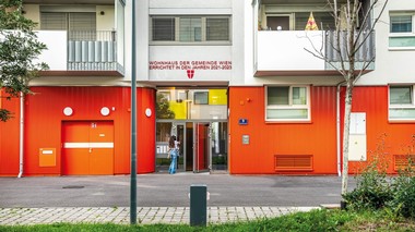 Außenansicht des Eingangbereichs. Das Erdgeschoss hat eine rote Fassade.
