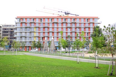 Foto der Außenansicht des neuen Gemeindebaus Seestadt Aspern. Die Fassade ist mit knalligen Farben wie Orange, Gelb, Blau und Grau gefärbt.