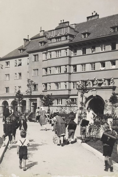 Schwarz-Weißaufnahme des Sandleitenhofs mit einigen Menschen, die sich vor dem Gemeindebau aufhalten