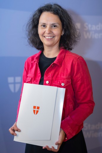 Katharina Klement hält ihr Bestellungsdekret mit dem Wiener Stadtwappen in der Hand und lächelt in die Kamera. Foto: © Stadt Wien / David Bohmann