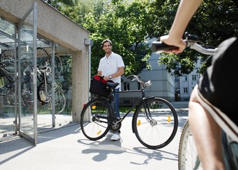 Foto einer Person mit Fahrrad, der vor einer Fahrradbox mit Glastür steht
