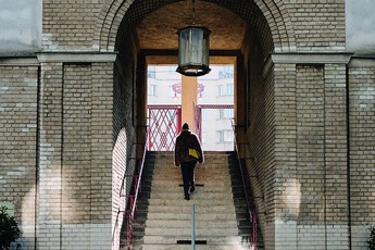 Eine Frau von hinten, die durch einen großen Torbogen die Stiege nach oben geht.