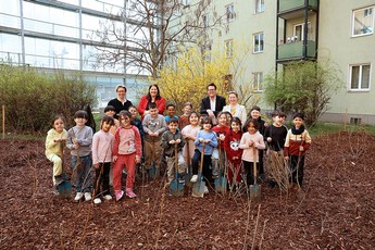 Das Bild zeigt eine Schulklasse und vier erwachsene Personen mit Schaufeln in einem gepflanzten Wald in einem Gemeindebau.