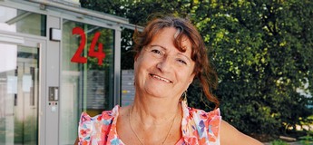 Foto einer lachenden Frau in einem sommerlichen T-Shirt, die vor einem Hauseingang steht