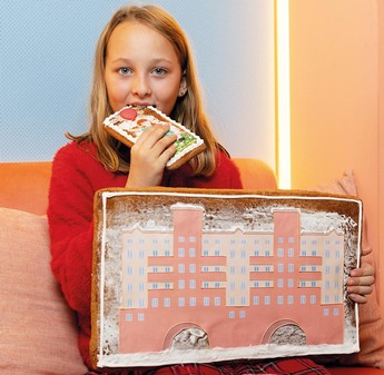 Das Foto zeigt ein blondes Mädchen, dass auf einer Couch sitzt und einen Lebkuchen ist. Der Lebkuchen hat die Form des Karl-Marx-Hofs.