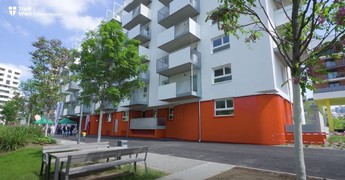 Foto eines neuen Gemeindebaus von außen mit einigen Balkonen und umgeben von einigen Bäumen und einer Grünfläche