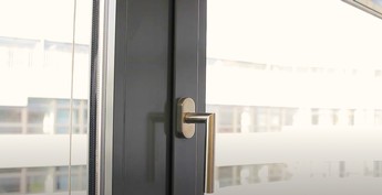 Man sieht einen Teil von einem Fenster mit grauem Rahmen und den Fenstergriff. Es geht um Lüften für die Schimmelvermeidung.