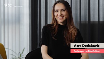 Eine Frau mit dunklen langen Haaren sitzt gemütlich auf einem Sessel und lacht in die Kamera.