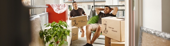 Zwei Männer sitzen mit Umzugskartons in einer Gemeindebauwohnung.