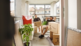 Zwei Männer sitzen mit Umzugskartons in einer Gemeindebauwohnung.