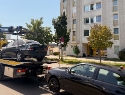 Ein Auto auf einem Abschleppwagen und eines das dahinter angehängt ist. Im Hintergrund ist ein Gemeindebau in Wien sichtbar.