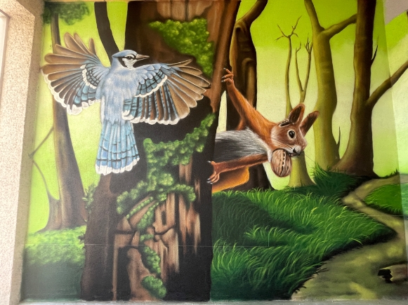Bild eines Kunswerkes, das einen blauen Vogel und ein Eichörnchen in einem Wald zeigt